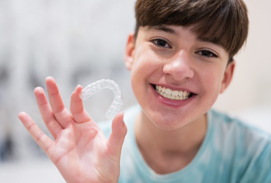 Teen smiling and holding a clear aligner tray showcasing invisible braces for teens in Europe by Smileie.