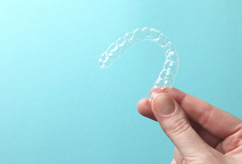 Clear dental retainer held in hand, used to prevent teeth shifting after aligners and maintain straight smile results