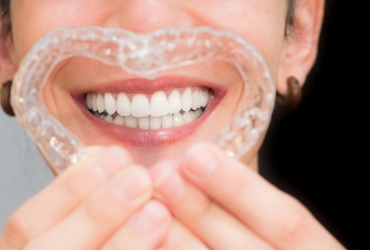 Person holding a clear dental aligner in front of a smiling mouth with straight white teeth