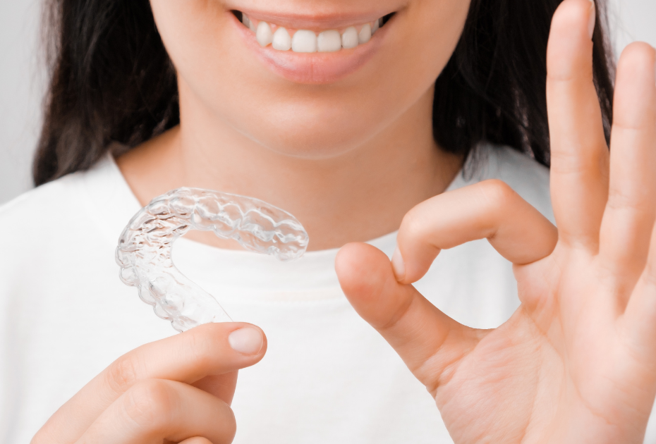 Person holding a clear aligner and smiling, showing invisible teeth straightening treatment.