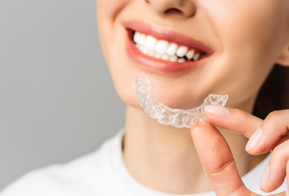 Woman holding clear aligners and smiling, demonstrating invisible teeth straightening treatment.