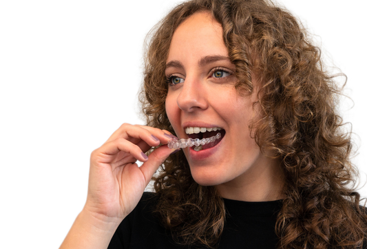 Student holding clear aligners while smiling in a university setting before starting teeth straightening treatment with invisible aligner trays.