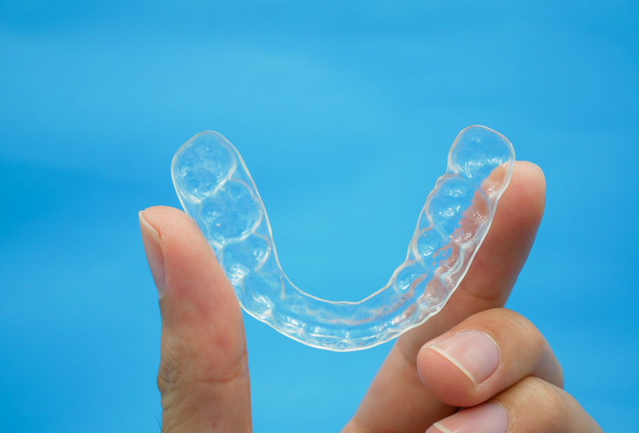 Hand holding a transparent dental aligner against a blue background